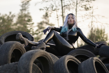 beautiful fetish woman lying on a huge pile of tires on the background of the sunset sky alone - obrazy, fototapety, plakaty