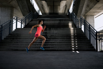 Side view of sporty young woman running on sidewalk in morning. Health conscious concept with copy...