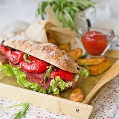 sandwich with ham, cream cheese, lettuce leaves, arugula, red pepper, baked potatoes, ketchup on a white wooden background with a floral fabric
