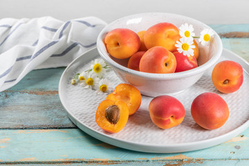 Delicious ripe apricots in a bowl on the wooden table. Close-up with apricots and daisy flowers