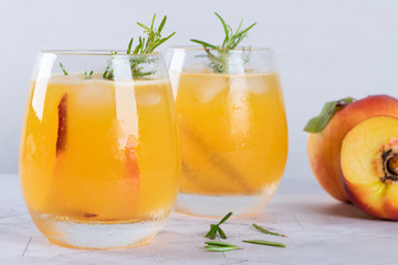 Homemade peach juice with ice cubes and rosemary leaves in glass on marble stone background.