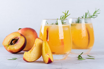 Homemade peach juice with ice cubes and rosemary leaves in glass on marble stone background.