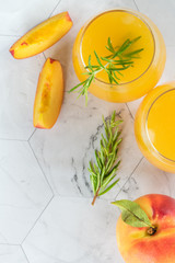 Homemade peach juice with ice cubes and rosemary leaves in glass on marble stone background.