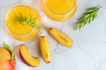 Homemade peach juice with ice cubes and rosemary leaves in glass on marble stone background.