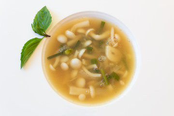 Mushroom garlic chive broth in white bowl garnished with basil, horizontal aspect