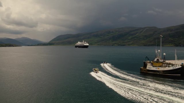 Silversea Cruises Silver Cloud anchored in Loch Broom, Ullapool, Ross-Shire, Highlands, Scotland with storm clouds building in the South with two fast moving boats in the loch.