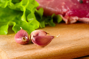 garlic peeled on a board with salad and meat for cooking