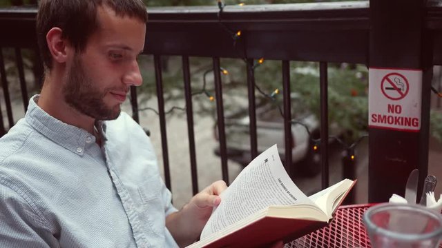 A Man reads a funny novel on a balcony near populated urban city area