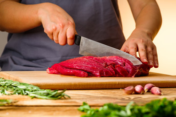 woman cuts fresh meat for cooking in the kitchen