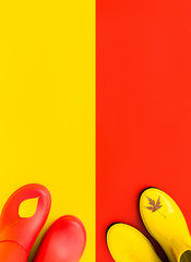 Red rubber boots to stand on a yellow background and the yellow boots are on a red background. And on toe's of boots there are autumn leaves.  The concept of 