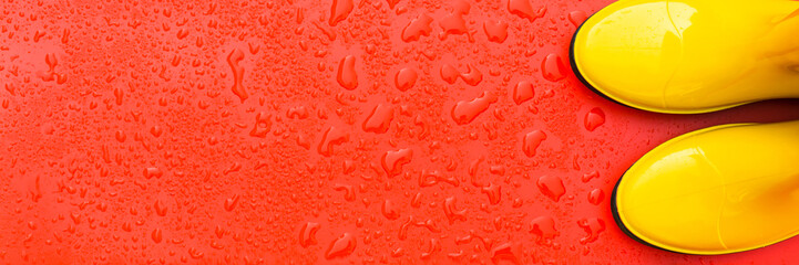 Red wet background and rubber yellow boots on it. Autumn background. Top view