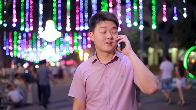 Asian boy talking at night in the Park, where a lot of lights. Gesturing, smiling and laughing a lot giving a good mood