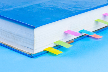 Close-up of pink post it note or sticky note, blue book with colorful label on blue background