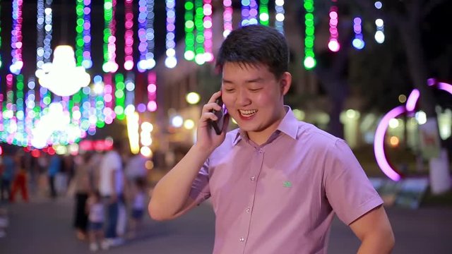Asian boy talking at night in the Park, where a lot of lights. Gesturing, smiling and laughing a lot giving a good mood