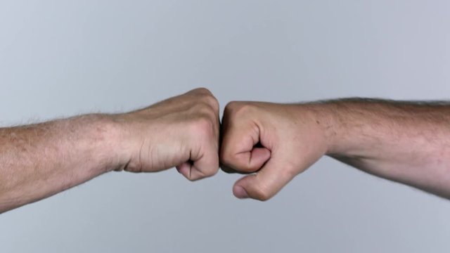 Two men fist bumping and making hands explode as they pull away against white screen.