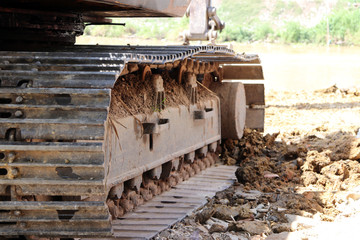Obraz premium closeup Continuous tracks or Tracked wheel of excavator or backhoe on the soil floor. The aggressive treads of the tracks provide good traction in soft or hard surfaces. To be driven.