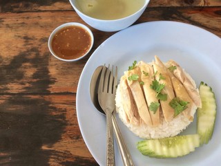 Hainanese chicken rice in blue plate , spoon and fork, soup with sauce on brown wooden table.