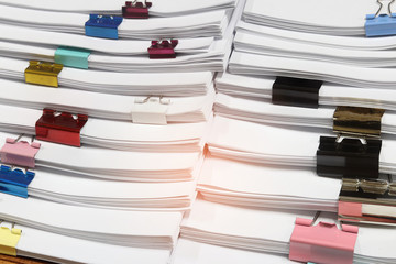 Close up pile of unfinished paperwork separated by colorful binder clips on office desk waiting to be managed. Stack of homework assignments. Report papers stacks. Business and education concept.