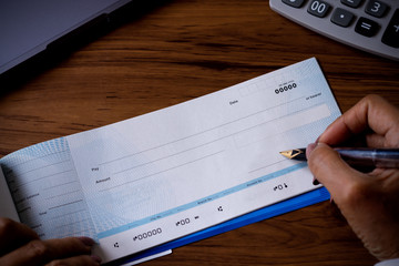 business woman hand writing cheque book with digital tablet and calculator on the wooden table at...
