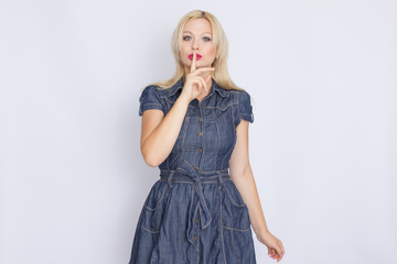 Studio portrait of a blonde woman in a denim dress. Girl posing on white background