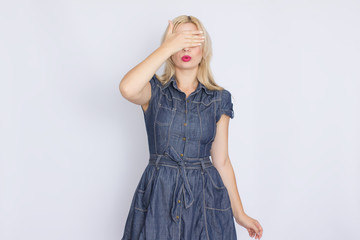 Studio portrait of a blonde woman in a denim dress. Girl posing on white background