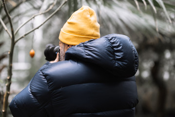 Mann mit gelber Mütze und blauer Jacke fotografiert eine Frucht im Botanischer Garten Schoenbrunn