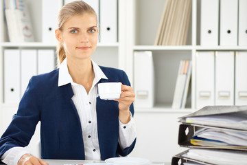 Happy business woman or female accountant having some minutes for coffee and pleasure at working place