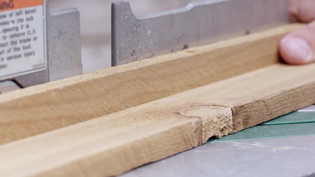 Close up view of board being cut by miter saw at an angle and cut pieces removed.