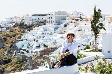 Fototapeta na wymiar Gourgeous view of blond woman in front of white walled town of Oia in Santorini, Greece