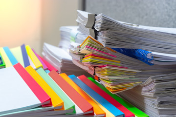 Close up pile of unfinished homework assignment on teacher's desk waiting to be inspected. Stack of paperwork separated by colorful paper clip and plastic binding bars. Education and business concept.