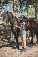 Woman enjoying horse company. Young Beautiful Woman dressed plaid shirt With black Horse Outdoors, stylish girl at american country style 