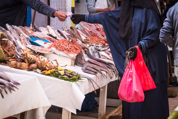 A woman in national Muslim clothing hijab pays for her purchases at the fish market in Essaouira. Morocco, Africa