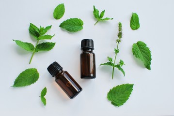 Essential oil of peppermint in brown bottles and fresh peppermint leaves on white background, flat lay. © IndrePau