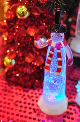 snow man clad with Red scarf and Black hat with bokeh lighting effect and Red Christmas Tree	