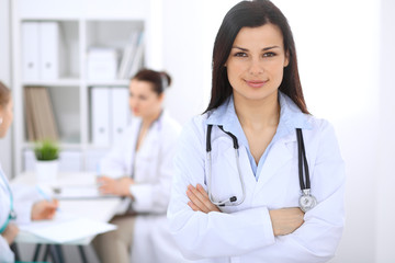 Fototapeta premium Brunette female doctor on the background of colleagues talking to each other in hospital. Medicine and health care concept