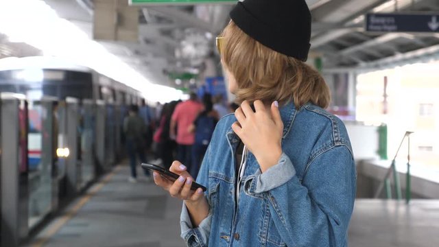 Woman Waiting On Station Platform Using Smart Phone