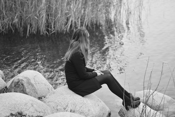 young girl sitting on the stones near the lake