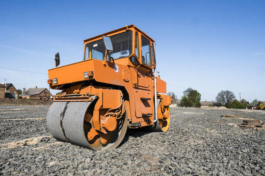 Orange light Vibration roller compactor standing on a stones at road construction and repairing asphalt pavement works with a blue sky.