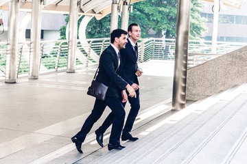 Two smiling businessman coworkers in black suit talking and walking.business people discussing strategy in the modern city