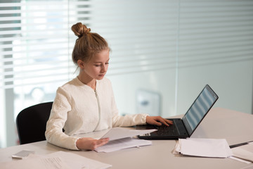 young girl businesswoman in casual clothes, sitting at a table closely look at documents, working at computer