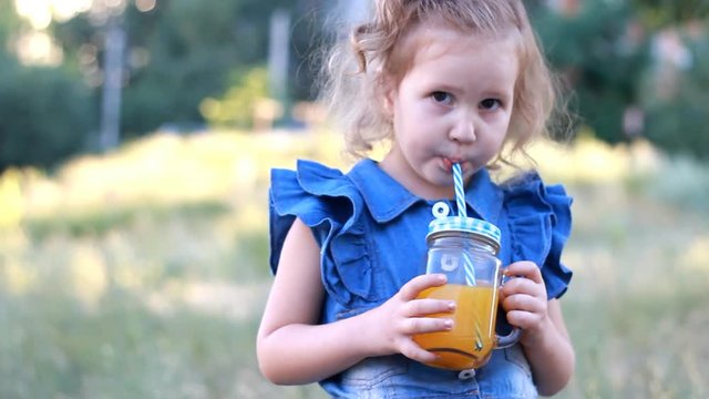 Child drinks orange fresh in the summer. Portrait of a little girl who enjoys smoothies through a tube