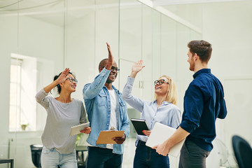 Ecstatic young office colleagues high fiving together in an offi