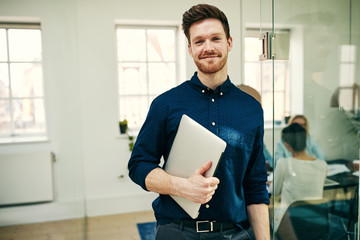 Smiling young businessman standing with his laptop at work