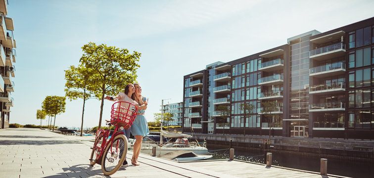 Smiling female friends standing with a bicycle in the city