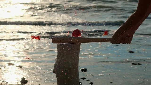 slow motion: young sexy girl beats a baseball bat with vegetables and a tomato fruit. It is located on the beach, sandy beach