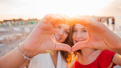 Two smiling girls (young women) making selfie photo on the beach with sunshine background.
