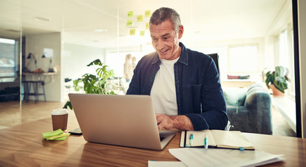 Smiling mature businessman using a laptop at his office desk