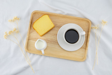 Fototapeta na wymiar A cup of coffee, milk and butter cake on wooden plate with flower on white bed