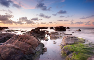 view of beautiful sunset at the beach with natural coastal rocks covered by green moss. soft focus due to slow shutter effect.