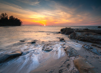 view of beautiful sunset at the beach with natural coastal rocks covered by green moss. soft focus due to slow shutter effect.